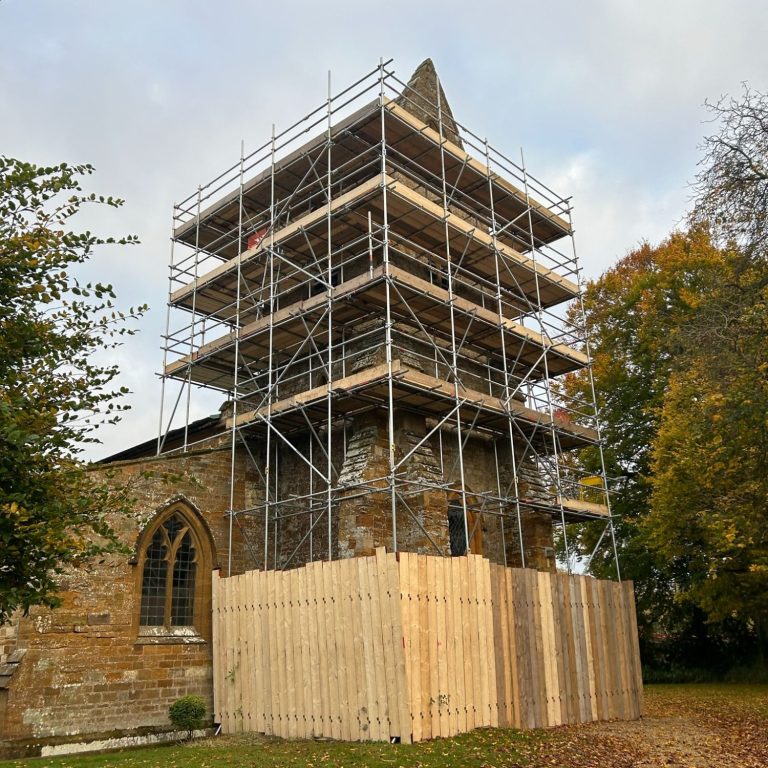 Rothersthorpe Church restoration scaffolding Stone church with scaffolding, surrounded by trees and autumn foliage.